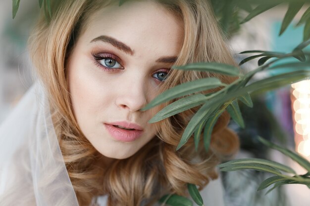 Portrait of young attractive girl with perfect skin among green leaves. 