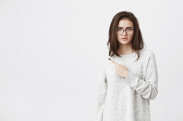 Portrait of young attractive model with angry and puzzled expression, pointing at upper left conner