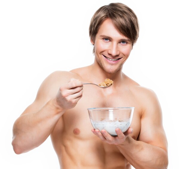 Portrait of a young attractive muscular man eating flakes with milk - isolated on white wall.