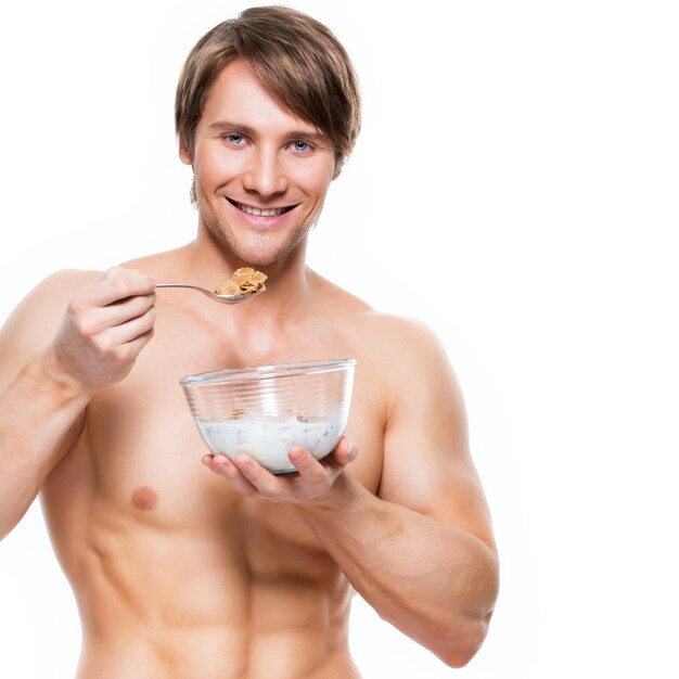 Portrait of a young attractive muscular man eating flakes with milk - isolated on white wall.