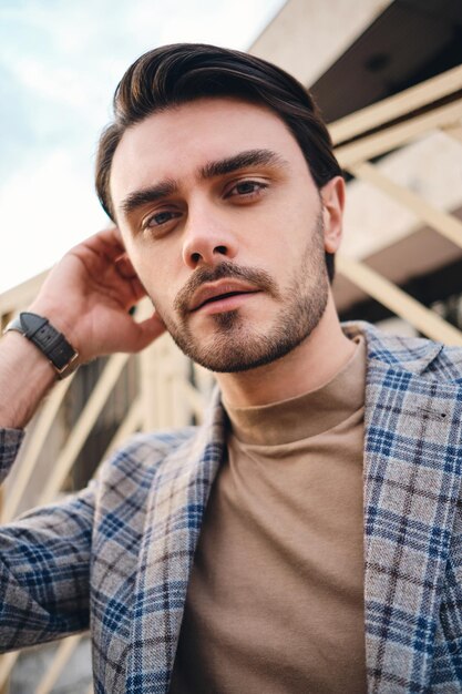 Portrait of young attractive stylish man in checkered jacket dreamily looking in camera outdoor