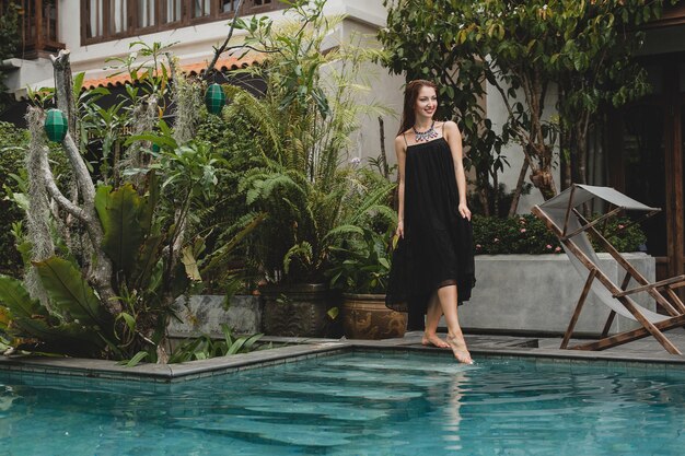 Portrait of young attractive woman in elegant dress, straw hat, summer style, fashion trend, vacation, smiling, stylish accessories, sunglasses, posing on tropical villa on Bali