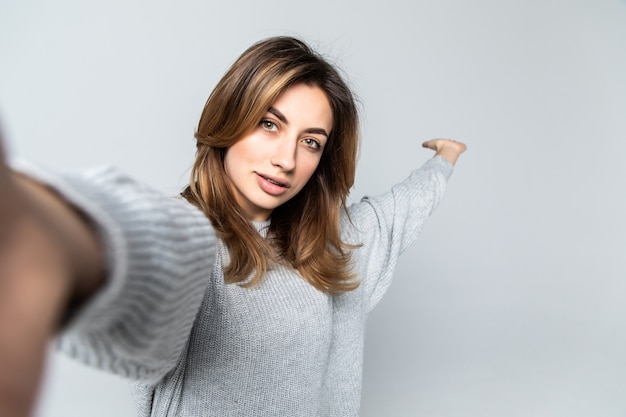Free photo portrait of a young attractive woman making selfie photo on smartphone isolated on a gray wall
