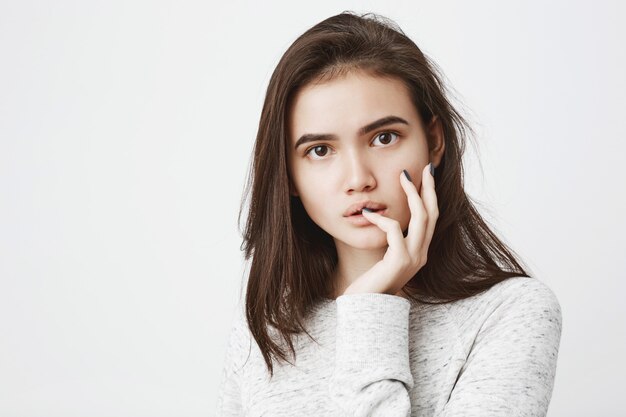 Portrait of young attractive woman with care haircut, looking with curiosity and touching lips