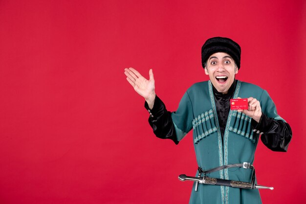 Portrait of young azeri man in traditional costume holding credit card on red