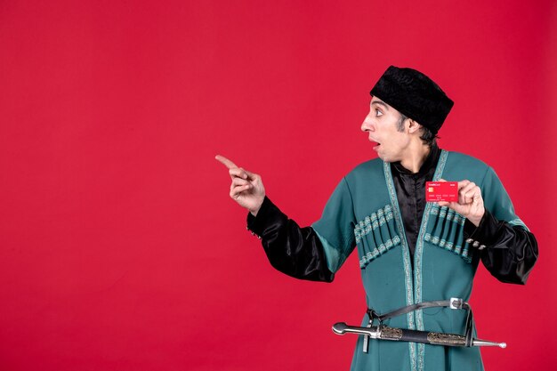 Portrait of young azeri man in traditional costume holding credit card on red