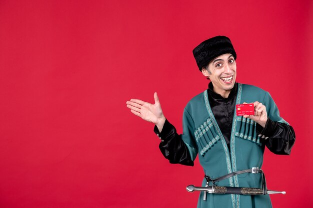 Portrait of young azeri man in traditional costume holding credit card on red