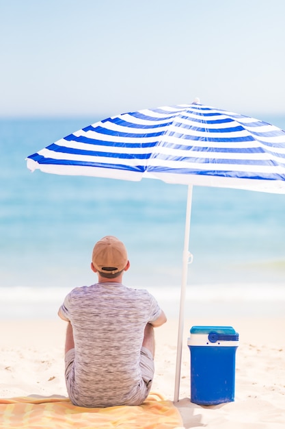 夏の日傘の下のビーチで若いひげの男の肖像画