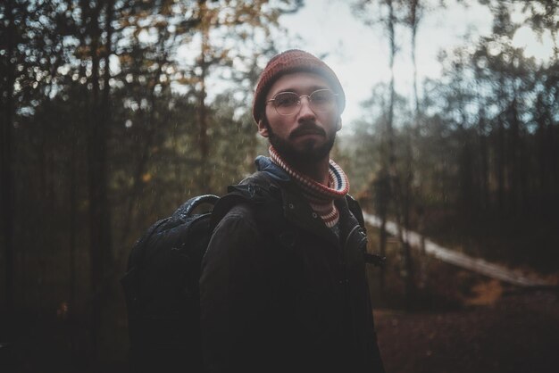 Портрет молодого бородатого хипстера с рюкзаком в осеннем лесу.
