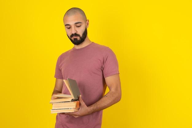 Portrait of a young bearded man holding books over yellow wall . 
