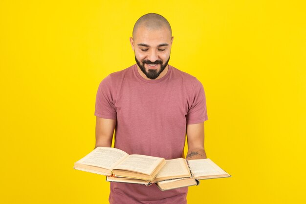 Portrait of a young bearded man holding opened books over yellow wall