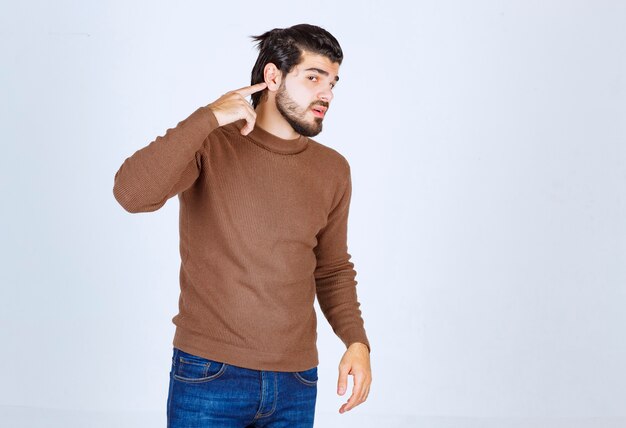 Portrait of a young bearded man pointing at ear with finger isolated on white wall . High quality photo