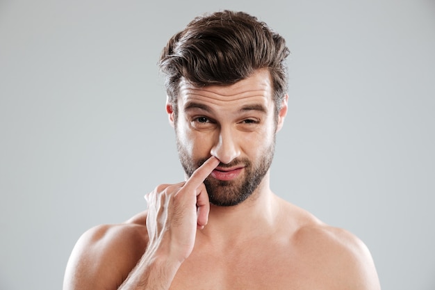 Portrait of a young bearded naked man picking his nose