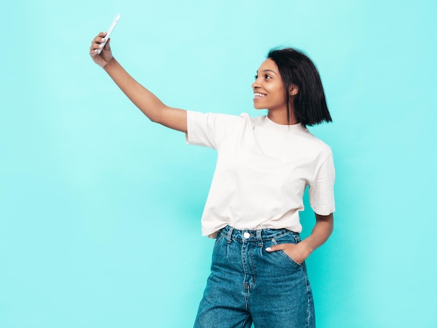 Portrait of young beautiful black woman Smiling model dressed in summer jeans clothes Sexy carefree female posing near blue wall in studio Tanned and cheerful