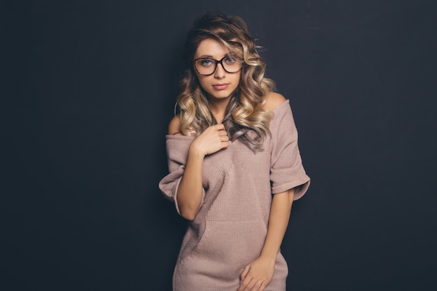 Portrait of a young beautiful blond-haired wearing trendy glasses and casual clothes and posing over black background