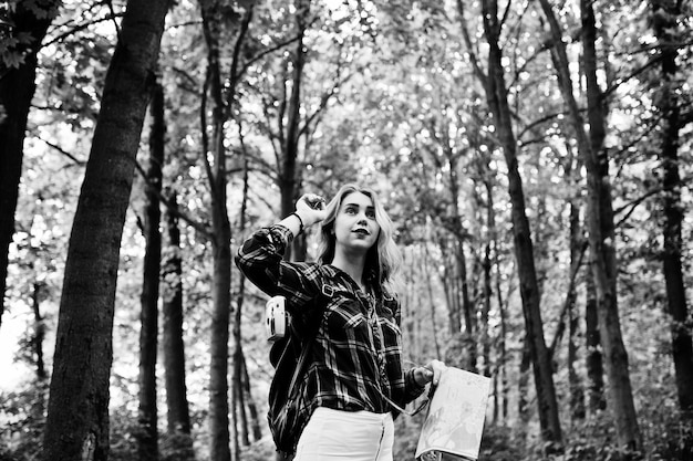 Portrait of a young beautiful blond woman in tartan shirt holding a map in the forest