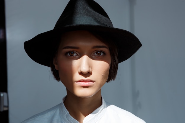 Portrait of young beautiful brunette girl in black hat.