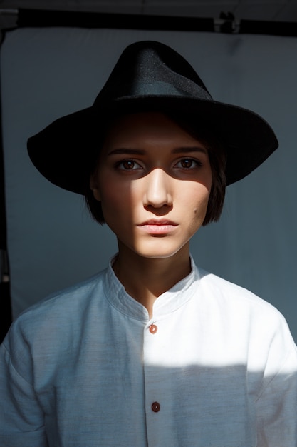 Portrait of young beautiful brunette girl in black hat.