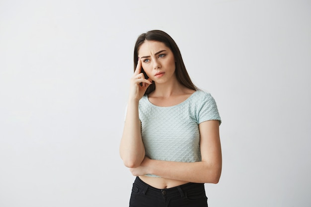 Portrait of young beautiful brunette girl frowning thinking with finger on temple .