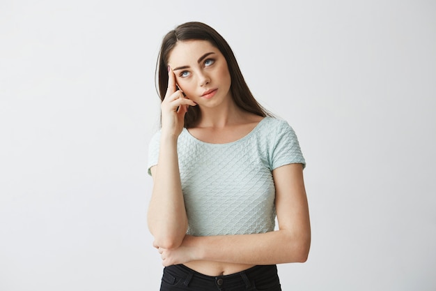 Portrait of young beautiful brunette girl frowning thinking with finger on temple .