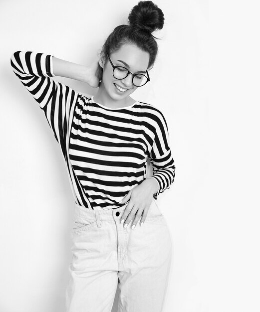 Portrait of young beautiful brunette woman girl model with nude makeup in glasses in summer hipster clothes posing near wall. 