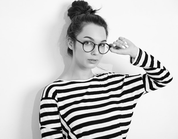 Portrait of young beautiful brunette woman girl model with nude makeup in glasses in summer hipster clothes posing near wall. 