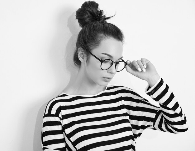 Portrait of young beautiful brunette woman girl model with nude makeup in glasses in summer hipster clothes posing near wall. 