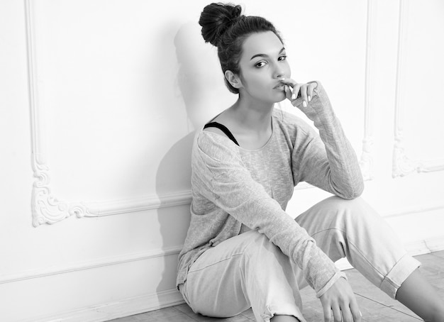 Portrait of young beautiful brunette woman girl model with nude makeup in summer clothes posing near wall. sitting in the floor