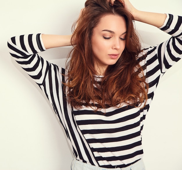 Portrait of young beautiful brunette woman girl model with nude makeup in summer hipster clothes posing near wall. touching her hair