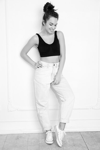 Portrait of young beautiful brunette woman girl model with nude makeup in summer T-shirt top and jeans clothes posing near wall. 