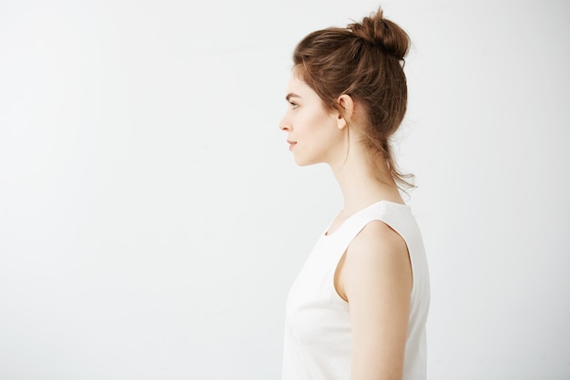 Portrait of young beautiful brunette woman with bun in profile smiling.