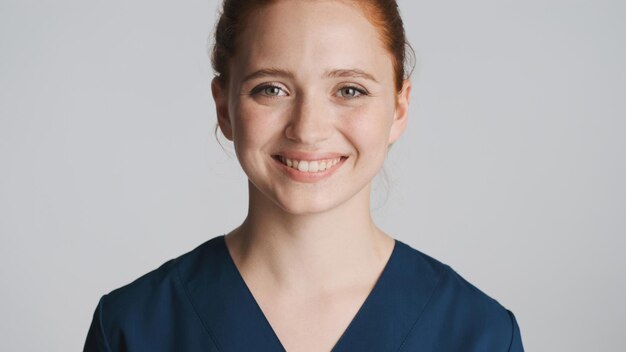 カメラで幸せそうに見て、白い背景に笑みを浮かべて若い美しい女性医師の肖像画