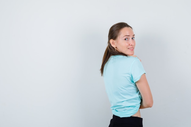 Portrait of young beautiful female looking over shoulder in t-shirt and looking joyful