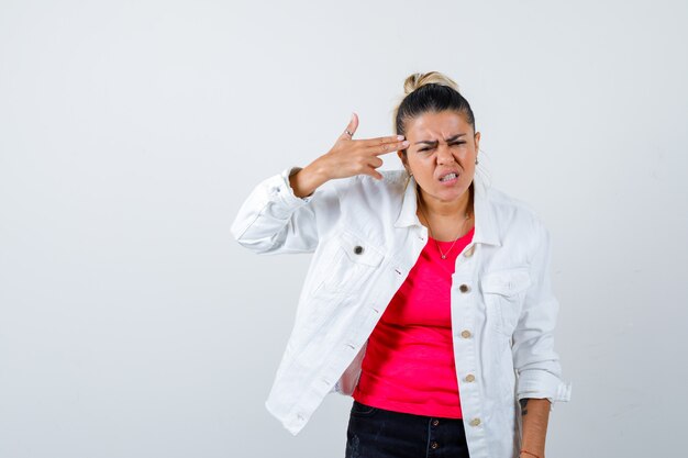 Portrait of young beautiful female making suicide gesture in t-shirt, white jacket and looking annoyed front view