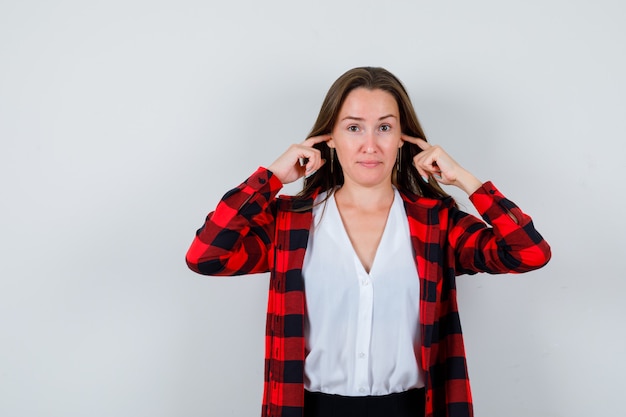 Free photo portrait of young beautiful female plugging ears with fingers in casual outfit and looking cheerless front view