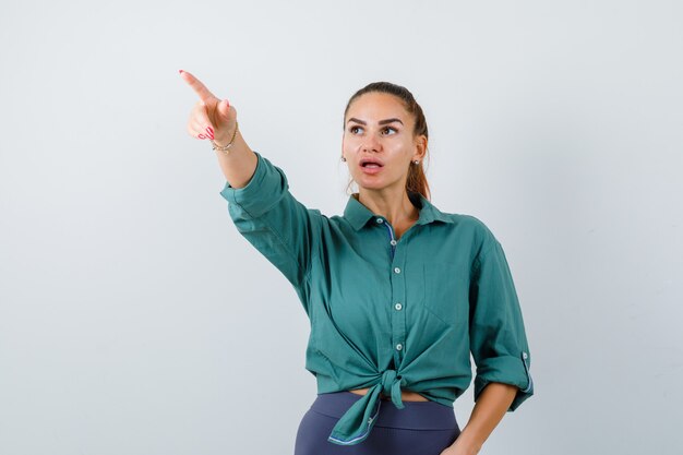 Portrait of young beautiful female pointing away in green shirt and looking bewildered front view