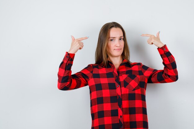 Portrait of young beautiful female pointing at herself in casual shirt and looking cheerless front view