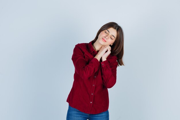 Portrait of young beautiful female posing while holding hand near face in shirt and looking sleepy