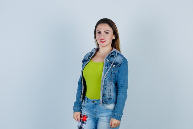 Portrait of young beautiful female posing while standing in denim outfit and looking cheerful front view