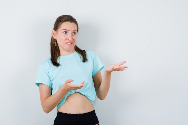 Portrait of young beautiful female pretending to show something in t-shirt and looking disgusted front view