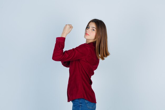 Portrait of young beautiful female showing arm muscles in shirt and looking confident