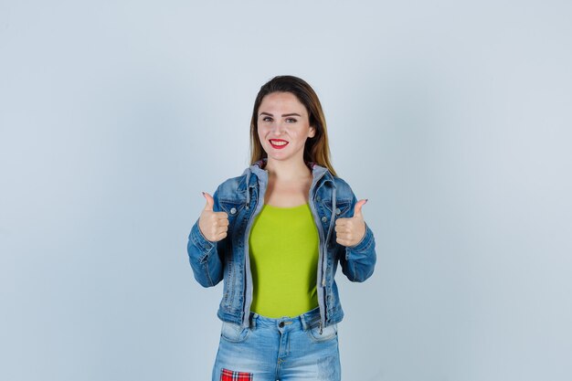 Portrait of young beautiful female showing thumbs up in denim outfit and looking merry front view