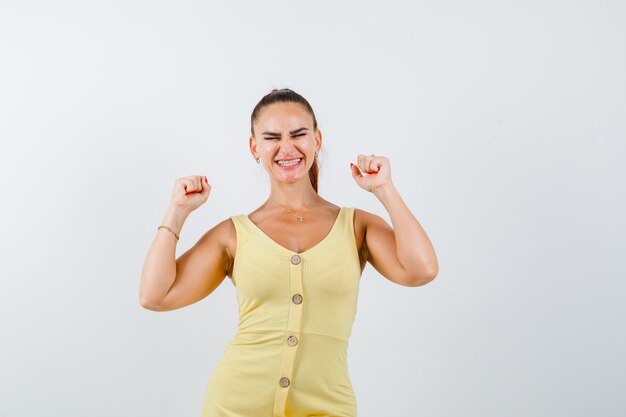 Portrait of young beautiful female showing winner gesture in dress and looking happy front view