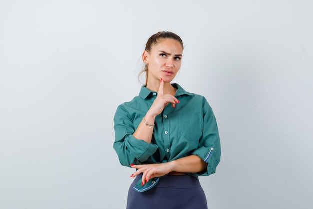 Portrait of young beautiful female standing in thinking pose in green shirt and looking puzzled front view