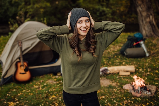 Portrait of young beautiful female tourist in the forest near tent and sleeping bag