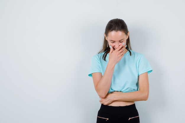 Free photo portrait of young beautiful female with hand on mouth in t-shirt and looking cheerful front view