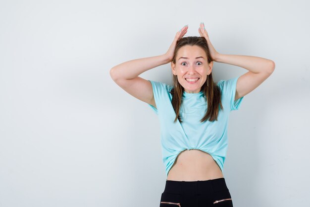 Portrait of young beautiful female with hands on head in t-shirt and looking cheerful front view