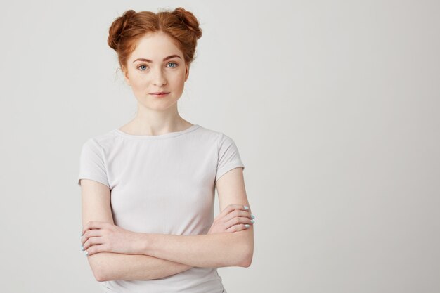 Portrait of young beautiful ginger girl with buns with crossed arms smiling .