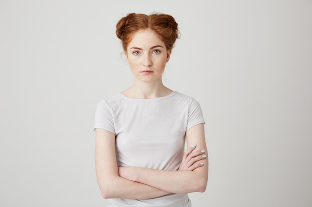Portrait of young beautiful ginger girl with buns with crossed arms .