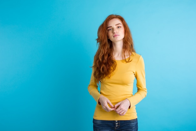 Portrait of young beautiful ginger woman with tender serious face crossing arms looking at camera. Isolated on pastel blue background. Copy space.